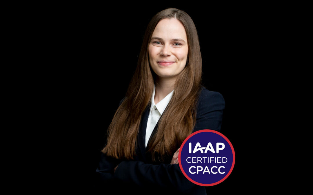 Alexandra Gurtner IAAP A smiling person with long hair and a suit stands with arms crossed, proudly displaying an IAAP Certified CPACC badge. Their dedication to accessibility is evident in their commitment to creating inclusive environments for all.